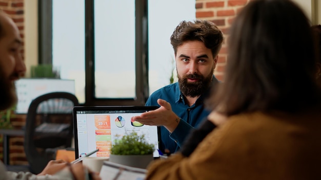 Free Photo project manager pointing at business charts on laptop, showing online research data to colleagues. people planning startup project and presentation with charts, creating successful report.