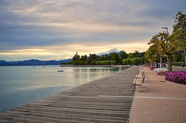 Promenade pier of Bardolino, lake Garda with benches, flowers, trees, water and dramatic evening sky