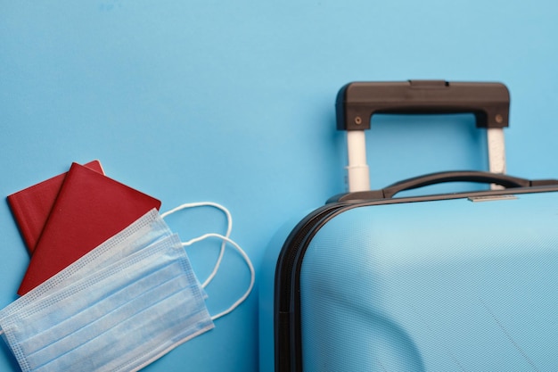 Free photo protective medical face mask and passport with suitcase on blue background top view