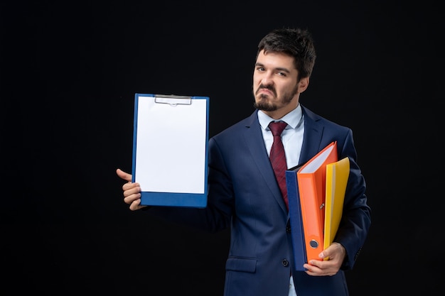 Free Photo proud adult in suit holding several documents and showing one of them on isolated dark wall