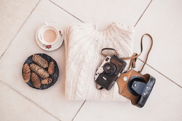 Pullover and camera laid near coffee and pinecones