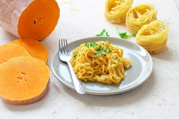 Free photo pumpkin alfredo fettucine pasta in a ceramic plate with fresh raw butternut squash slices. autumn meal for lunch. butternut squash recipe