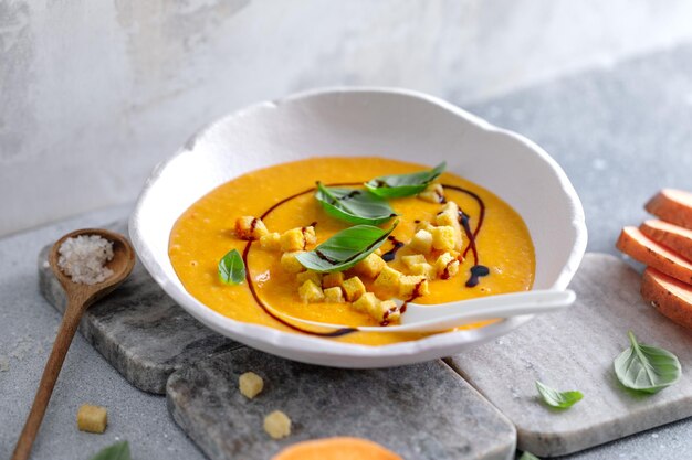 Pumpkin mashed soup with croutons and basil served in bowl on table