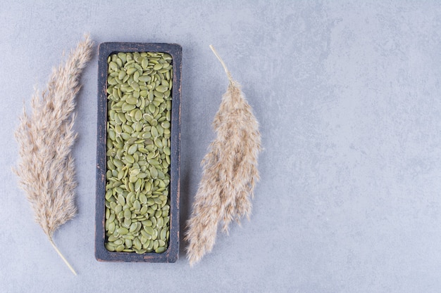 Free photo pumpkin seed in a wooden plate next to pampas grass on marble.