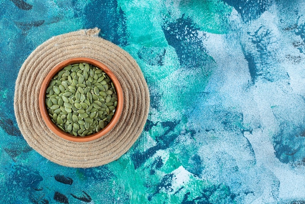 Free photo pumpkin seeds in a bowl on trivet on marble.