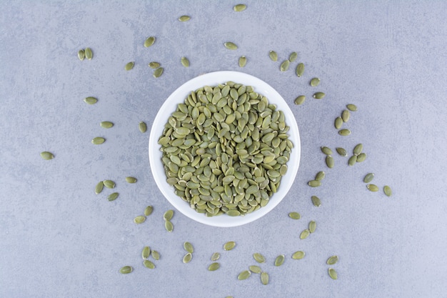 Free photo pumpkin seeds in a bowl on trivet on marble.