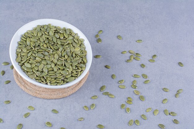 Pumpkin seeds in a bowl on trivet on marble.