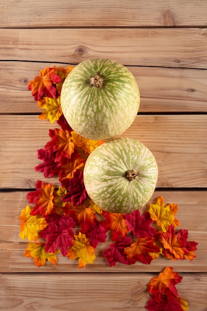 Pumpkin with leaves on wooden table, top view