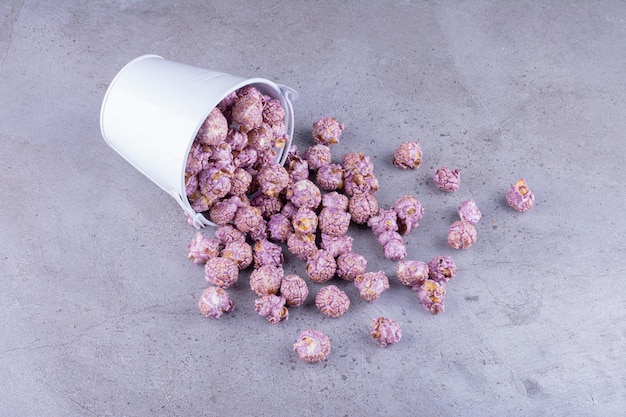 Free photo purple candied popcorn pouring out of a bucket on marble background. high quality photo