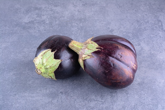 Purple eggplants isolated on concrete background.