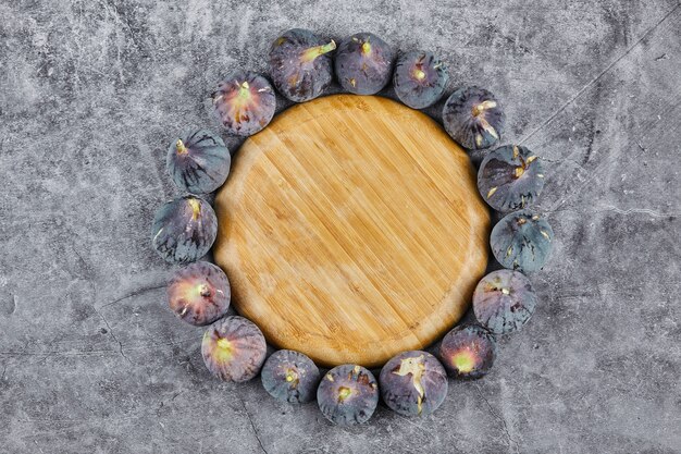 Purple figs around a wooden plate on marble.