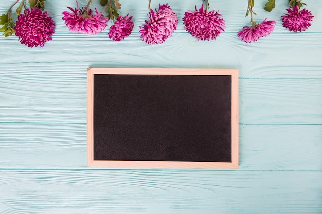 Free photo purple flowers with blank chalkboard on blue wooden table