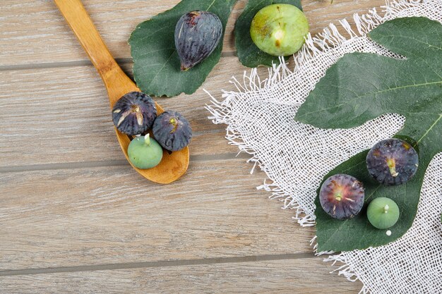 Purple and green figs on wooden table with a white tablecloth, a leaf and a wooden spoon.