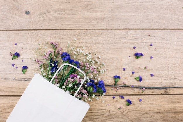 Purple limonium and gypsophila flowers inside the white shopping bag on wooden desk