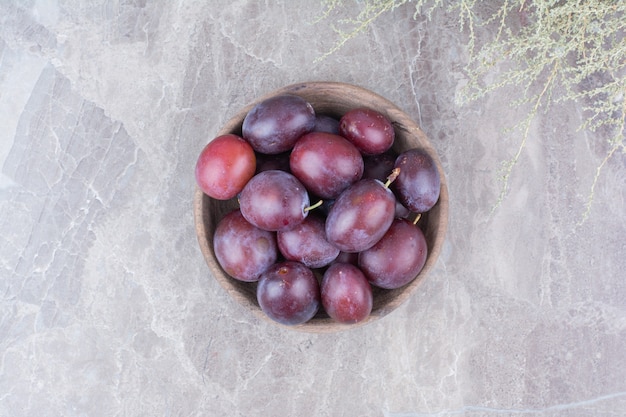 Free photo purple plums in wooden bowl on stone background.