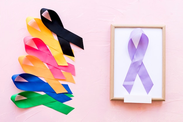 Purple ribbon on white wooden frame with the row of colorful awareness ribbon