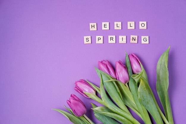 Purple tulips on a violet background and wooden letters Spring concept Top view flat lay copy space