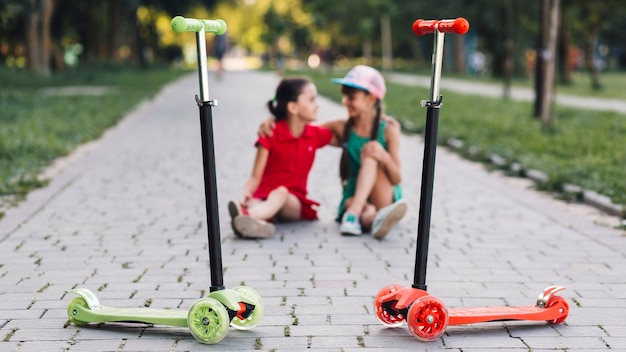 Push scooters in front of girls sitting on walkway in the park