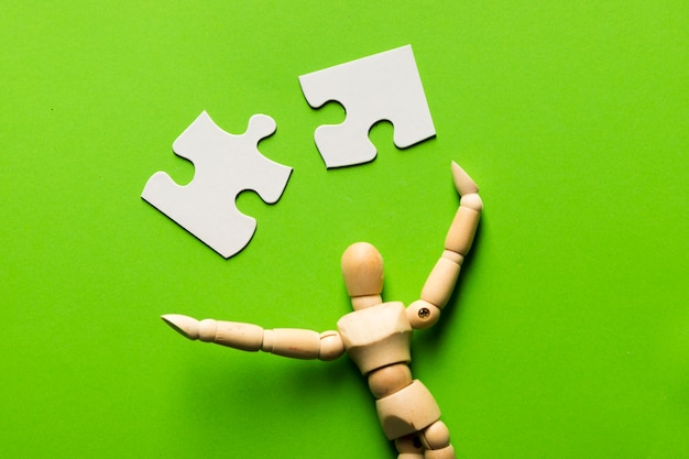 Free Photo puzzle piece with wooden human figure on green backdrop