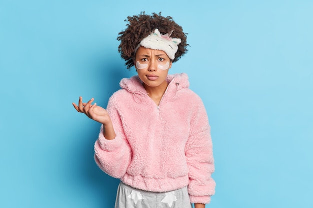 Puzzled Afro American woman looks with bewilderment raises palm feels confused