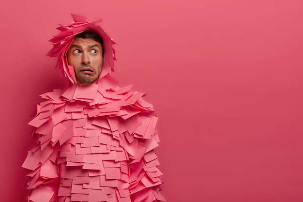 Free Photo puzzled guy concentrated somewhere, thinks how to solve situation, has indignant face expression, purses lips, covered with pink stickers around head and body copy space away for your promotional text