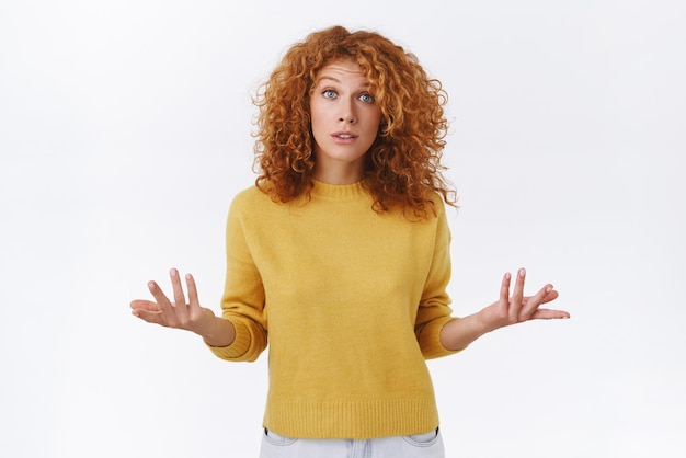 Free Photo puzzled indecisive cute redhead curly woman in yellow sweater have misunderstanding raise arms and shrugging troubled lift eyebrows in surprise standing questioned uncertain white background