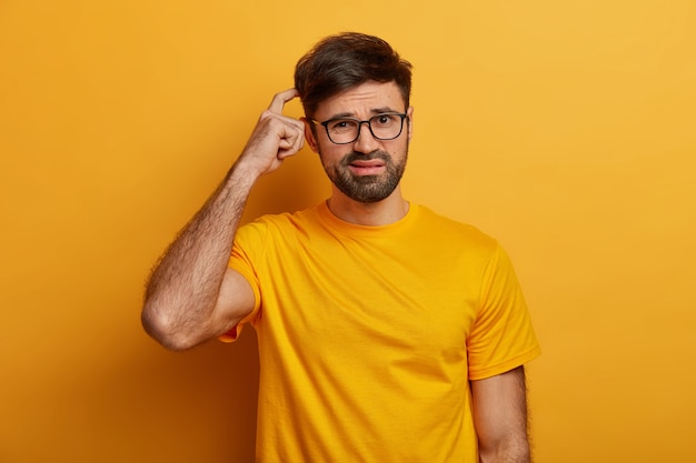 Free photo puzzled indecisive man scratches head, has no idea