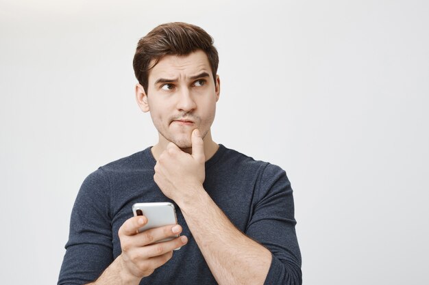 Puzzled thoughtful man thinking while holding smartphone