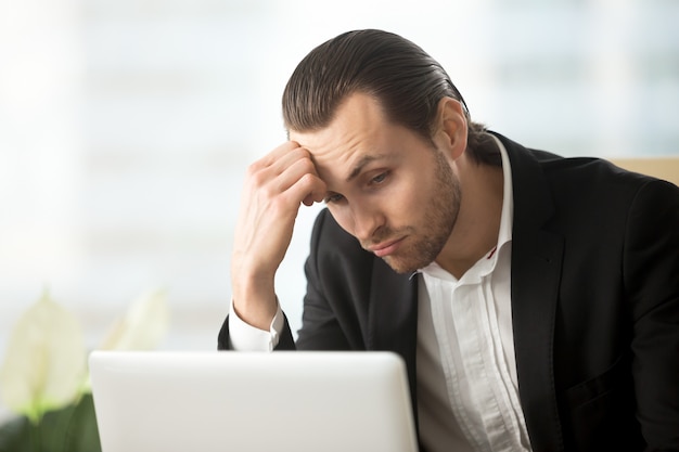 Puzzled young businessman looking at laptop screen 