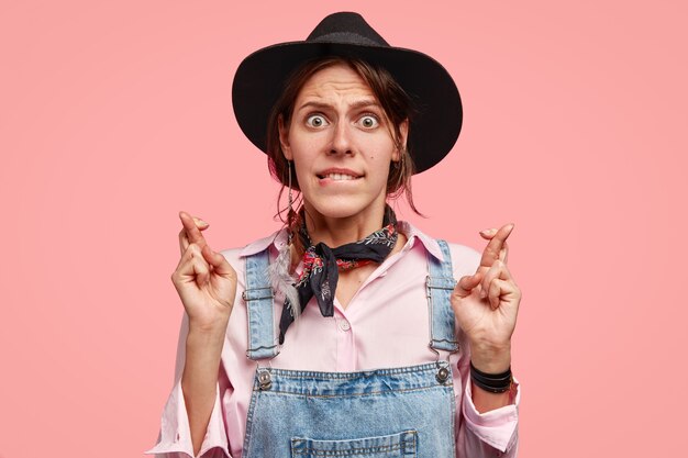 Puzzled young European gardener bites lower lip, keeps fingers crossed, waits for important results