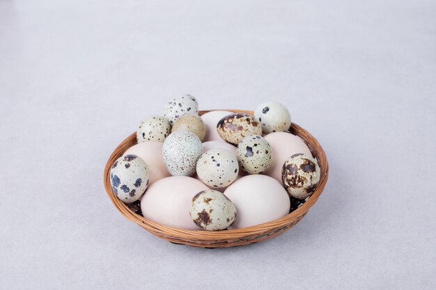 Quail eggs and chicken eggs in bowl on white surface.