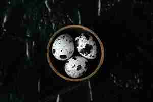 Free photo quail eggs. raw quail eggs in container. three quail eggs on black background