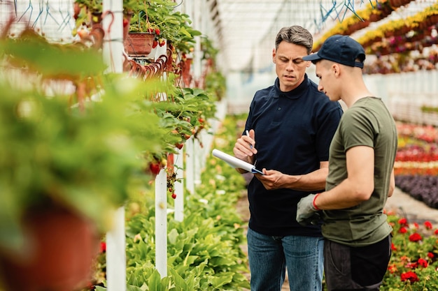 Quality control inspector and worker talking while going through list of plants in a greenhouse