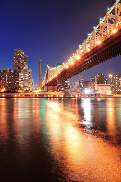 Queensboro Bridge over New York City East River at sunset with river reflections and midtown Manhattan skyline illuminated.