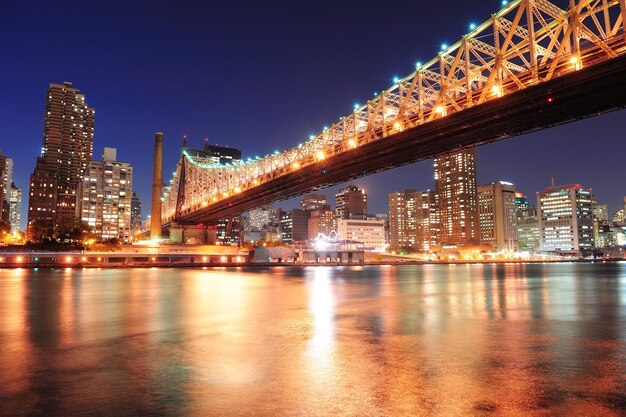 Queensboro Bridge over New York City East River at sunset with river reflections and midtown Manhattan skyline illuminated.