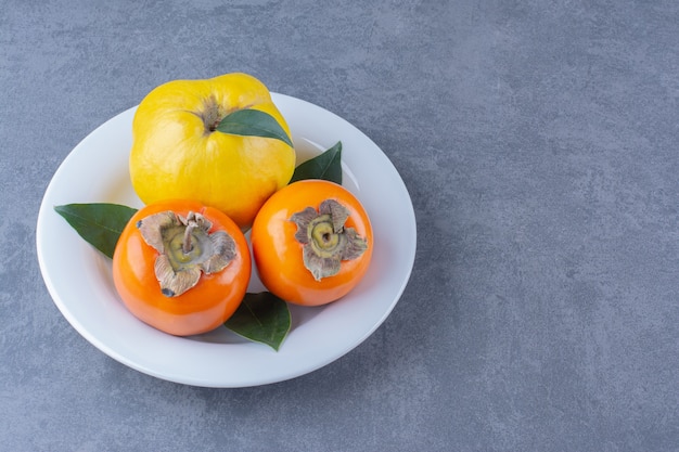 Quince and persimmon fruits on plate on the dark surface