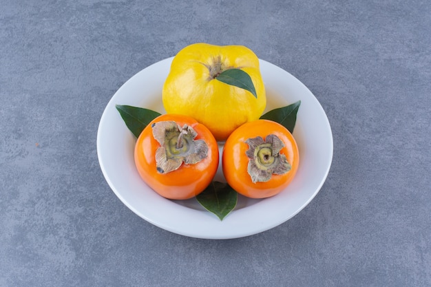 Quince and persimmon fruits on plate on the dark surface