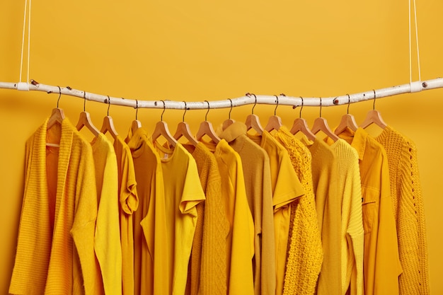 Free photo rack with yellow clothes after dry cleaning. wardrobe with various outfits for different seasons. womens wear in fashion shop. selective focus. blank space above.