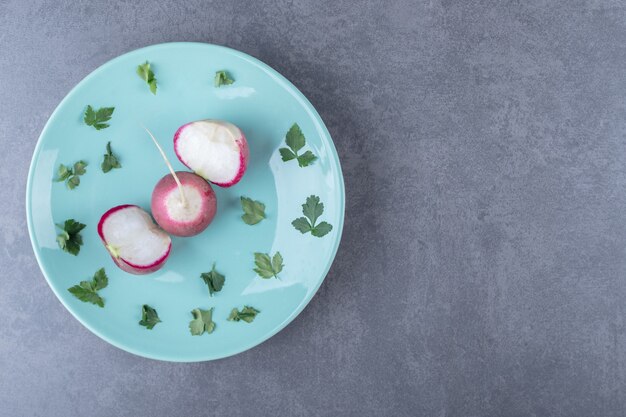 Radish and greenery on the plate , on the marble surface.