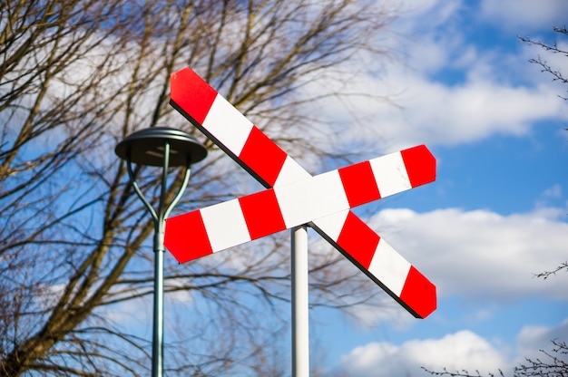 Free photo railway crossing sign against bare trees and cloudy blue sky