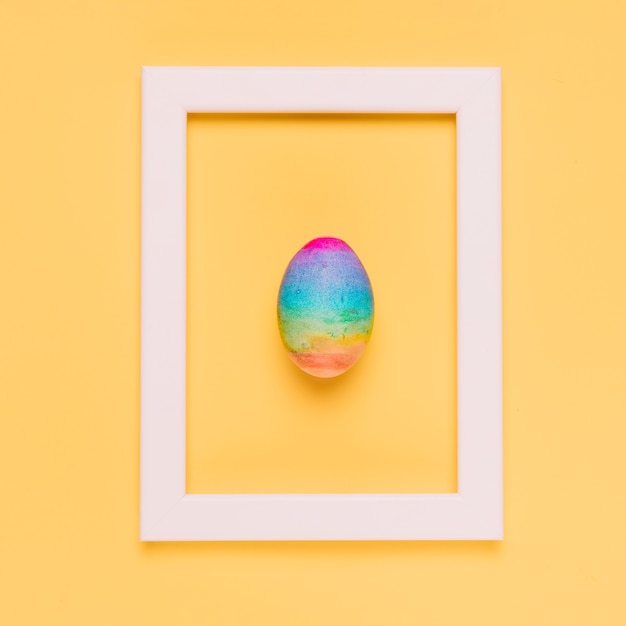 Free photo rainbow color easter egg inside the white border frame on yellow background