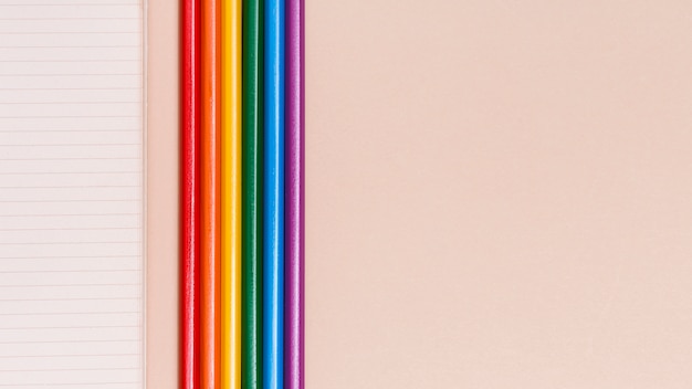 Rainbow colorful pencils and notebook on beige background