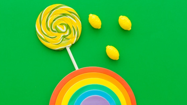 Free photo rainbow near lollipop and lemon candies on green background