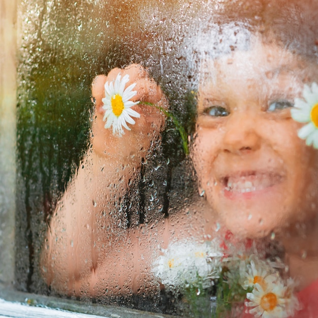 Raindrops on the glass of a village window, chamomile flowers eyes in children's hands look at the rain.