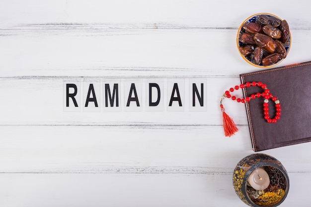 Ramadan text with bowl of juicy dates; diary and red prayer beads on white table