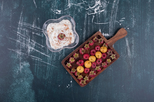 Free photo raspberries and cherries in a wooden platter with a glass of icecream in the center