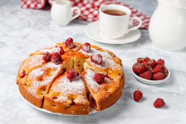 Raspberry cake with powdered sugar and fresh raspberries on a light . Summer berry dessert.