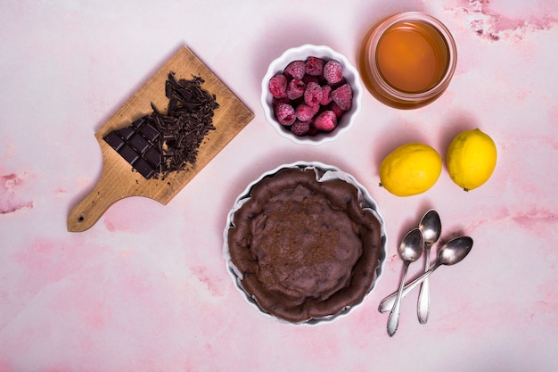 Raspberry; lemon; oil; chocolate bar with fresh prepared cake and spoons on pink textured background