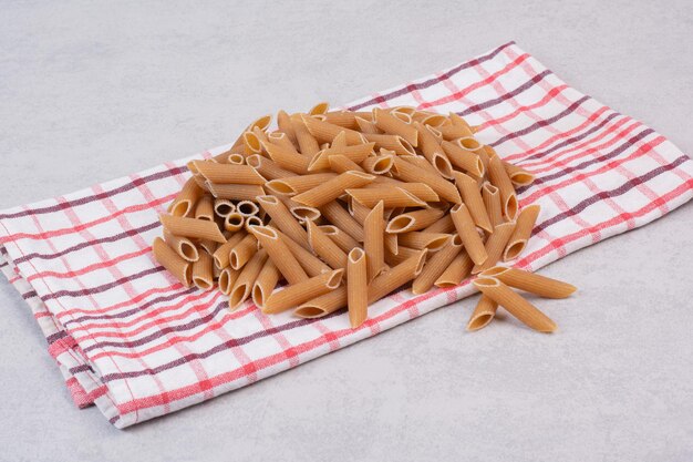 Raw brown penne pasta on striped tablecloth.