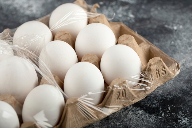 Free photo raw chicken eggs in egg box on a marble surface.